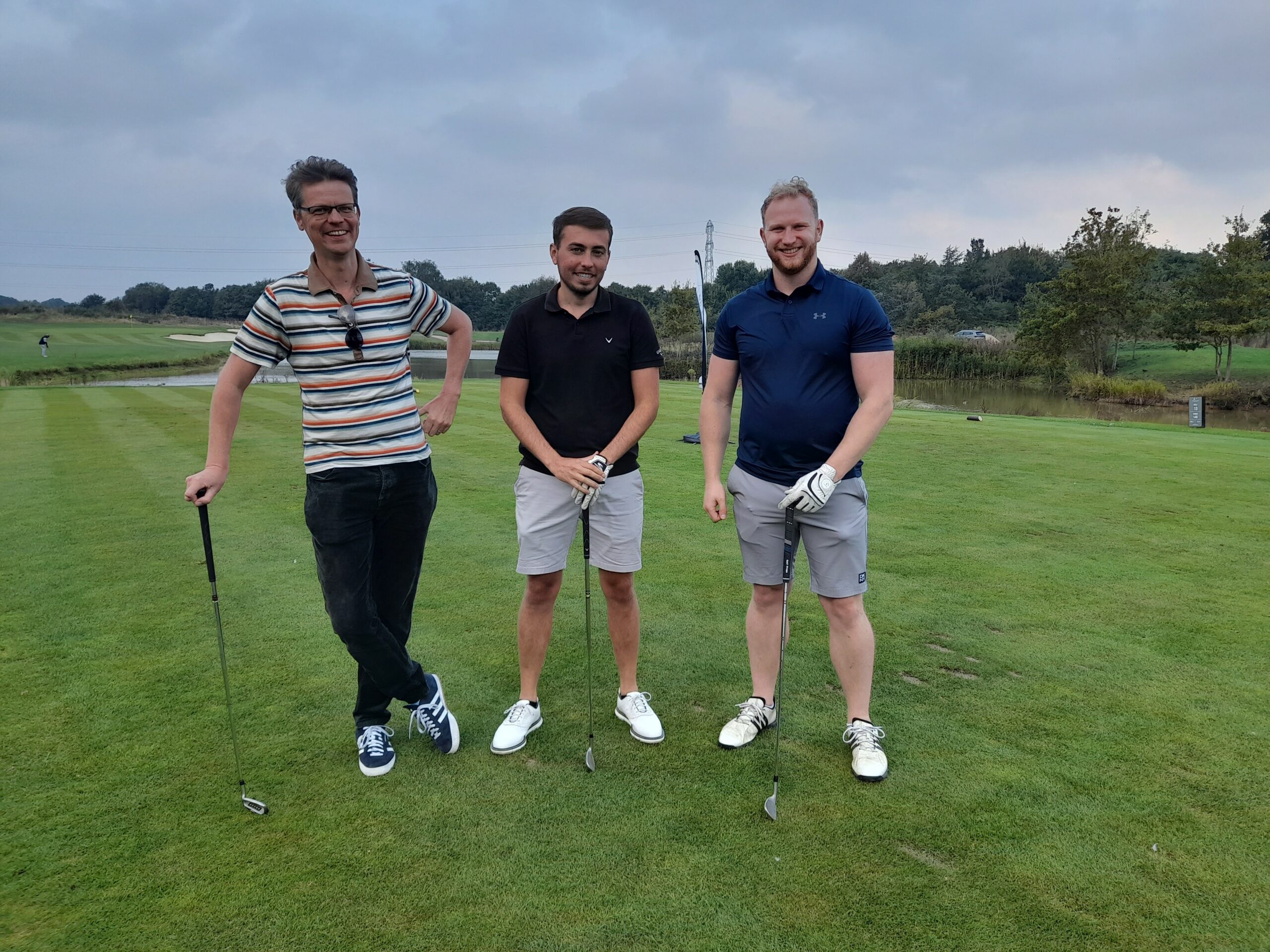 Three members of staff from Look Ahead and AD Construction standing on a golf course with their golf clubs.